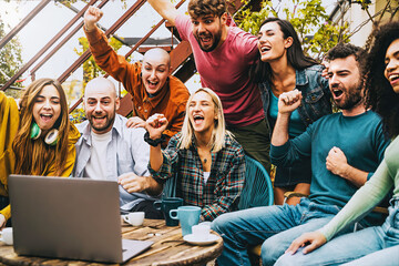 Group of multiethnic international people celebrating raising arms for for a goal watching contents in streaming on a laptop computer