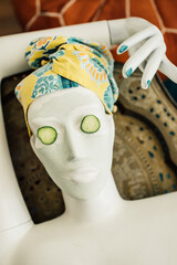 day at the spa: mannequin bust with green clay face mask, cucumber slices on eyes, yellow towel...