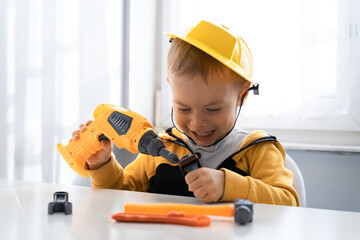 Obraz na płótnie Canvas Child play with work tools at home, dreams to be an engineer. Little boy builder. Education, and imagination, purposefulness concept. Kid and drill