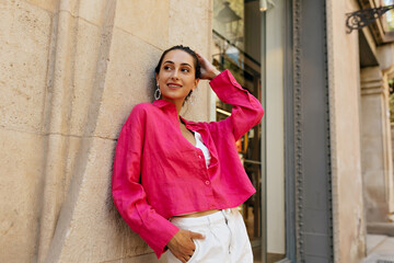 Slender stylish girl modestly poses for photo against beige wall. Smiling lady in summer pink...