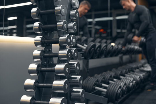 Rows of dumbbells in the gym. Modern sports gym. Rows of dumbbells and a bodybuilder blurred on the background