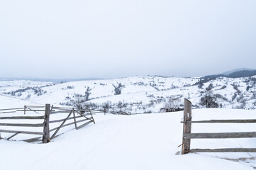 Wooden gate in the snowy mountains. Snow-capped mountains and fields. Winter in the mountains. Entrance and exit to the mountains.