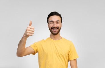 Naklejka premium young latin man smiling at camera with thumbs up. white background