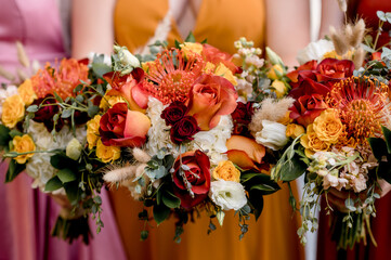 Bridesmaids in autumn colors holding colorful bouquets filled with orange roses and yellow anemones, close up crop no faces
