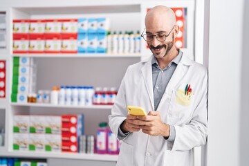 Young hispanic man pharmacist using smartphone standing at pharmacy