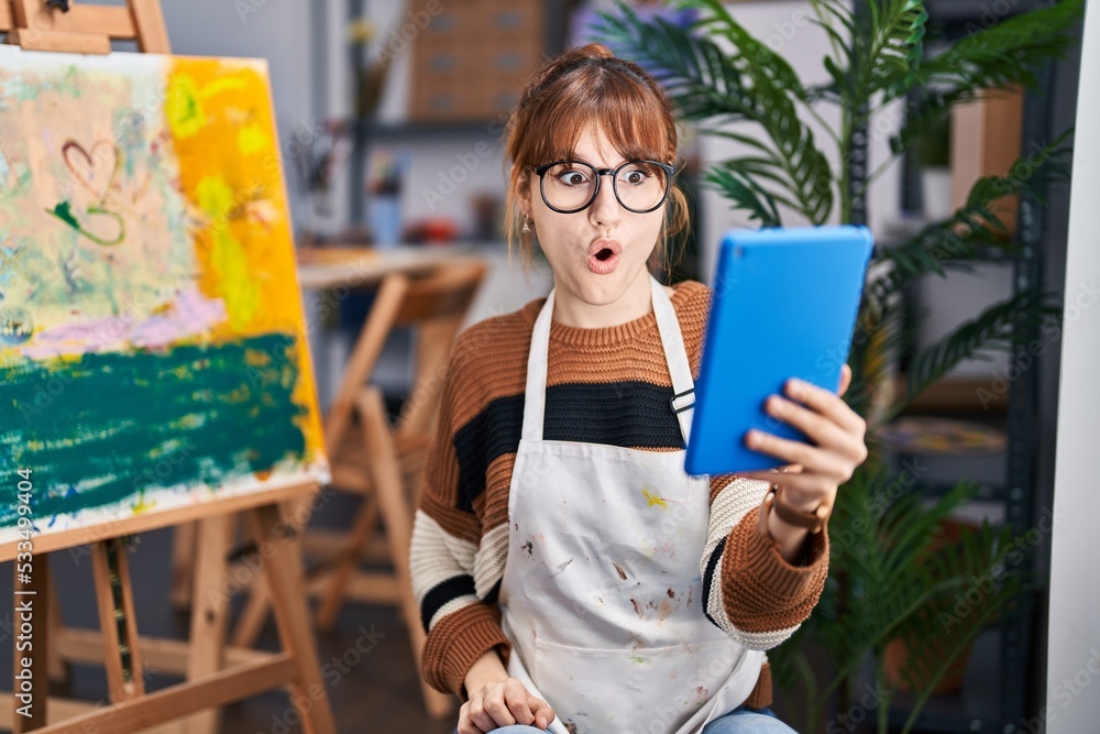 Sticker Young beautiful artist woman doing video call with tablet scared and amazed with open mouth for surprise, disbelief face