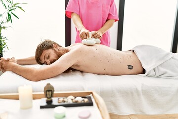 Obraz na płótnie Canvas Young redhead man having back massage using thai bags at beauty center