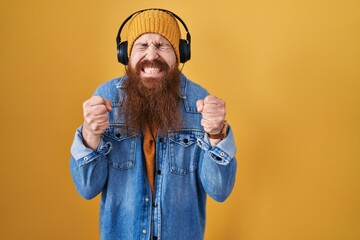 Caucasian man with long beard listening to music using headphones excited for success with arms raised and eyes closed celebrating victory smiling. winner concept.