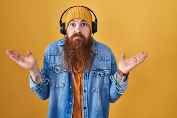Caucasian man with long beard listening to music using headphones clueless and confused expression...