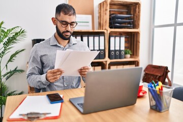 Naklejka premium Young hispanic man business worker using laptop reading document at office