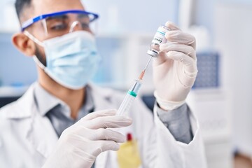 Young hispanic man scientist holding covid vaccine at laboratory