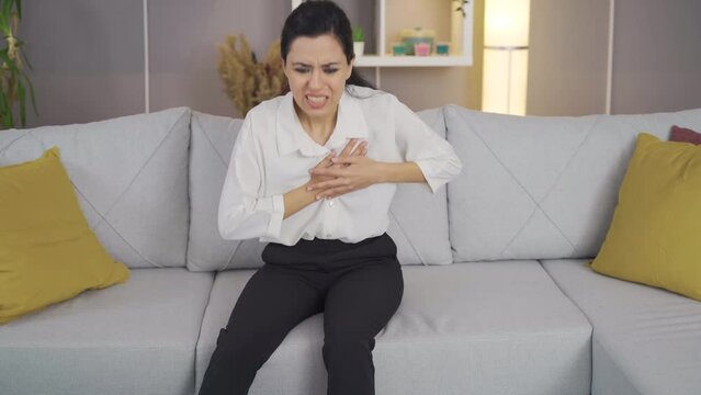 Young woman experiencing heartache at home.
Young woman in pain holding her heart, her heart aches.

