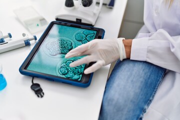 Young blonde woman wearing scientist uniform looking embryion images at laboratory
