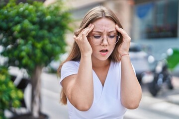 Young blonde woman suffering headache standing at street