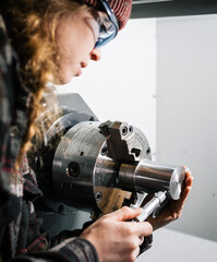 Industrial woman machinist uses a CNC lathe machine and a micrometer for calibration