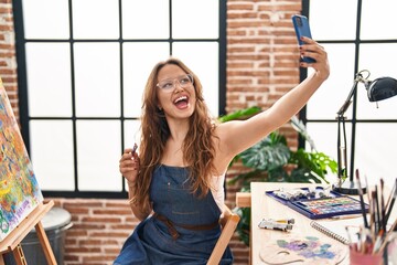 Young beautiful hispanic woman artist make selfie by smartphone at art studio
