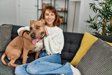 Young caucasian woman smiling confident hugging dog sitting on sofa at home