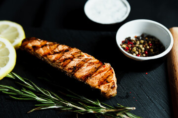 Grilled salmon fish fillet with green salad on the black cutting board, close up. Delicious food in the restaurant menu. Concept of catering service