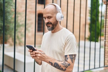 Young bald man listening to music with serious expression at street