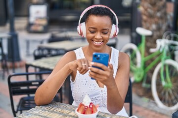 African american woman eating ice cream listening to music at coffee shop terrace
