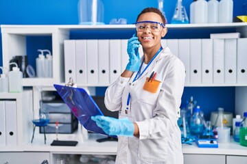 African american woman scientist talking on smartphone reading document at laboratory