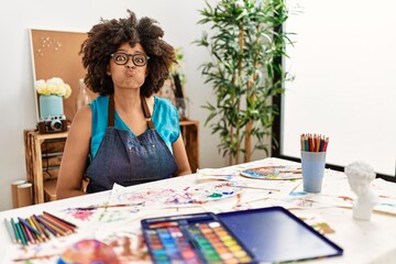 Beautiful african american woman with afro hair painting at art studio puffing cheeks with funny face. mouth inflated with air, crazy expression.