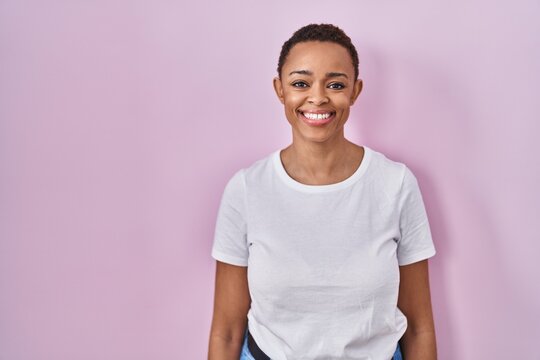 Beautiful african american woman standing over pink background with a happy and cool smile on face. lucky person.