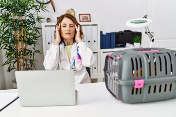 Middle age veterinarian woman working at pet clinic with hand on head for pain in head because...