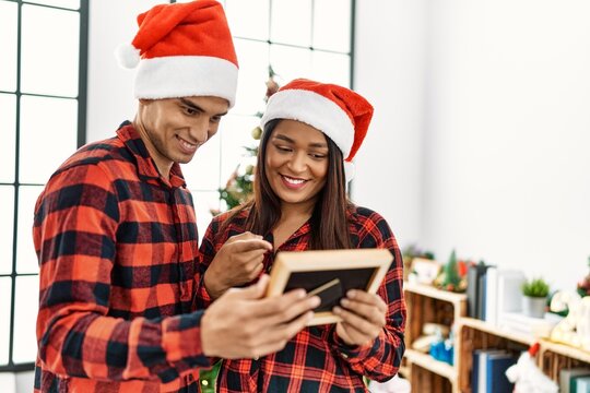 Young latin couple celebrating christmas holding frame at home.