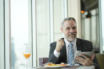 Caucasian Businessman using tablet computer. Happy middle aged man sitting in a restaurant. Entrepreneur working online, reading finance report, thinking.