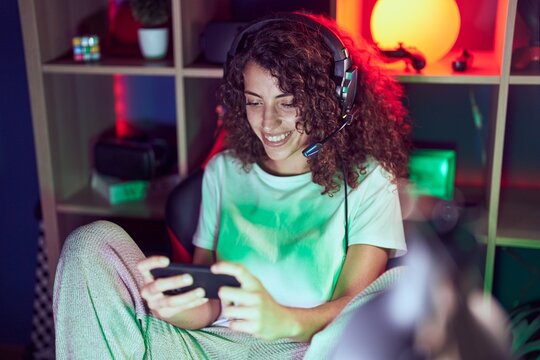 Young beautiful hispanic woman streamer playing video game using smartphone at gaming room