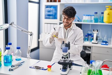 Young hispanic man scientist smiling confident writing on test tube at laboratory