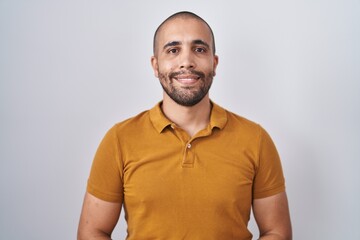 Hispanic man with beard standing over white background with hands together and crossed fingers smiling relaxed and cheerful. success and optimistic