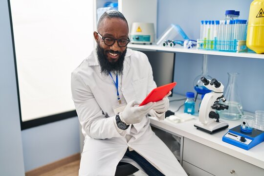 Young african american man wearing scientist uniform using touchpad at laboratory