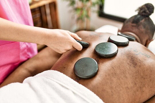 Young african american man having back massage with hot stones at beauty center