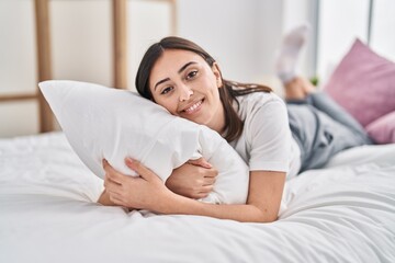 Young hispanic woman hugging pillow lying on bed at bedroom