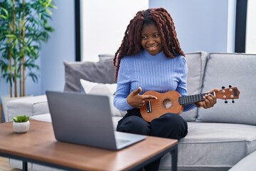 African woman playing ukulele at home doing video call smiling happy pointing with hand and finger