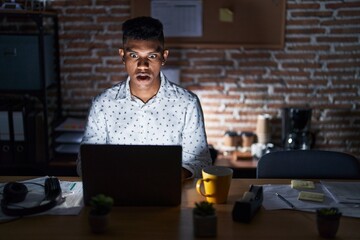 Young hispanic man working at the office at night afraid and shocked with surprise expression, fear...