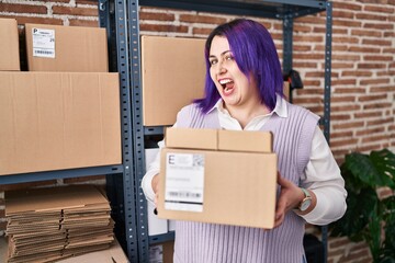 Plus size woman wit purple hair working at small business ecommerce holding boxes angry and mad screaming frustrated and furious, shouting with anger. rage and aggressive concept.
