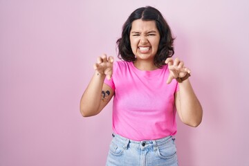 Obraz na płótnie Canvas Young hispanic woman standing over pink background smiling funny doing claw gesture as cat, aggressive and sexy expression