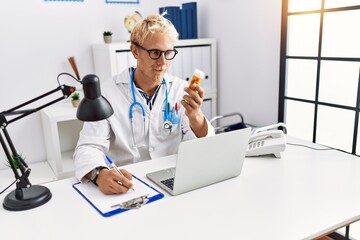 Obraz premium Young caucasian man wearing doctor uniform holding pills at clinic