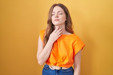 Caucasian woman standing over yellow background touching painful neck, sore throat for flu, clod and infection
