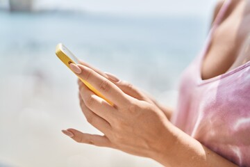 Young blonde woman using smartphone at seaside