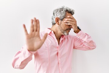 Middle age hispanic man standing over isolated background covering eyes with hands and doing stop...