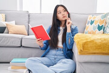 Young chinese woman reading book with doubt expression at home