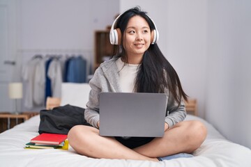 Young chinese woman listening to music sitting on bed at bedroom