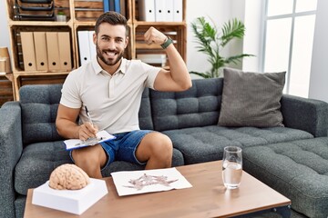 Handsome hispanic man working with rorschach test at psychology clinic strong person showing arm...