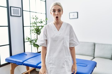 Young caucasian physiotherapy woman working at home scared and amazed with open mouth for surprise, disbelief face