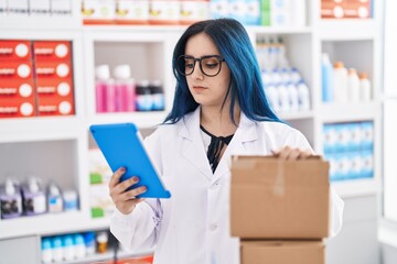 Young caucasian woman pharmacist using touchpad holding packages at pharmacy