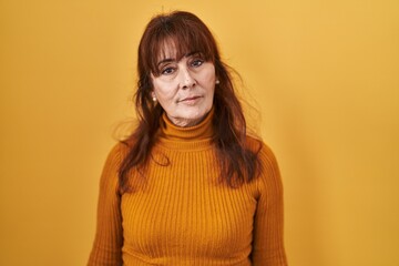 Middle age hispanic woman standing over yellow background relaxed with serious expression on face. simple and natural looking at the camera.